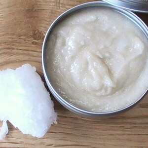 May include: A small metal container filled with a white, creamy substance. A separate white, solid lump of the same substance is on a wooden surface.