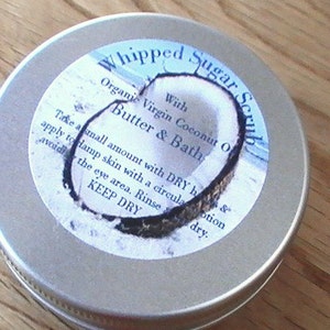 May include: A silver tin with a white label that reads "Whipped Sugar Scrub with Organic Virgin Coconut Oil Butter & Bath". The label also includes instructions for use and the words "Keep Dry".