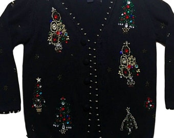 Op de afbeelding: Zwarte gebreide cardigan met een V-hals en knoopsluiting. De trui is versierd met kleurrijke kerstboomversieringen van kralen en gouden sterren.
