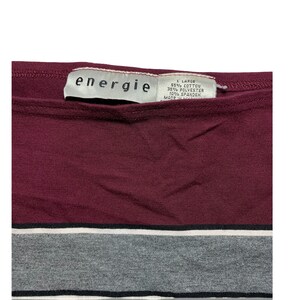 Peut inclure: Un t-shirt ray&eacute; marron et gris avec une &eacute;tiquette blanche qui indique "energie" et "L Large 55% Coton 35% Polyester 10% Spandex Made in Jordan".