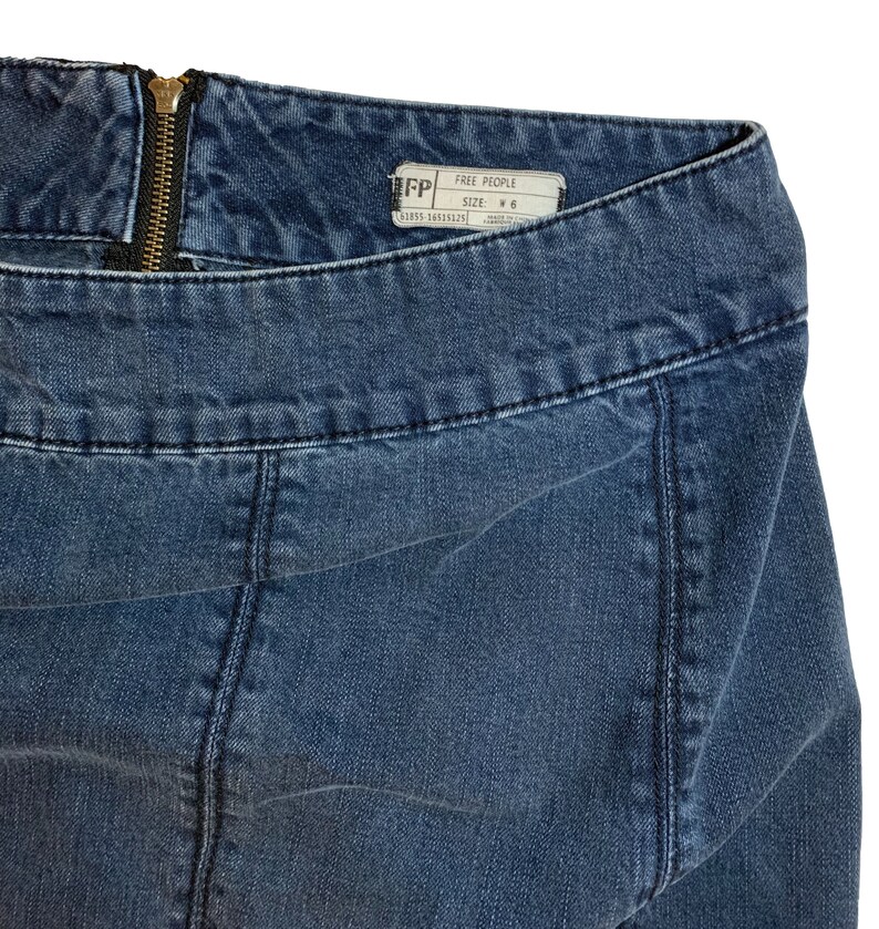Pu&ograve; includere: Un paio di jeans blu denim con zip e un'etichetta Free People che dice "Free People" e "Taglia: W6".