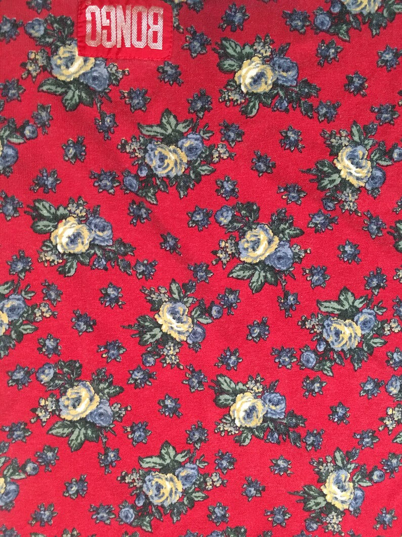 May include: Red fabric with a floral pattern featuring small blue and yellow flowers. The fabric has the word "BONGO" printed in white letters on a red background.