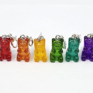 May include: A row of six gummy bear keyrings in red, orange, yellow, green, teal, and purple. Each bear-shaped charm has a silver-tone clasp. The keyrings are displayed against a white background.