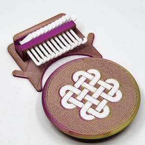 May include: A 3D-printed craft tool set, featuring a purple and gold-coloured weaving loom and a round coaster with a white Celtic knot design. The loom has white teeth and a purple frame. The coaster is approximately 10 cm in diameter.