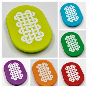 May include: A selection of oval coasters in shades of green, blue, purple, orange, and red. Each coaster displays a white Celtic knot pattern. The coasters are made from a solid material and are suitable for drinks. Each coaster is approximately 10 cm long.