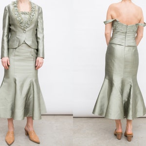 May include: A two-piece outfit in a light green color. The top is a fitted jacket with a lace trim collar. The skirt is a mermaid style with a fitted waist and a flowing bottom.