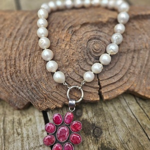 Può includere: Una collana di perle bianche con un ciondolo d'argento a forma di fiore rosa con otto pietre di rubino.