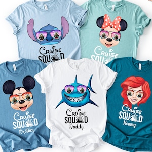 May include: Five short-sleeved t-shirts in light blue, mint green, medium blue, white, and teal. Each shirt features a cartoon character wearing sunglasses with a cruise ship reflection and the text Cruise Squad, including Stitch, Minnie Mouse, Mickey Mouse, a shark, and Ariel.