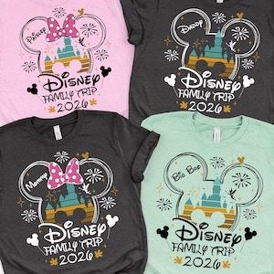 May include: Four short-sleeved t-shirts in pink, charcoal, and mint green. Each shirt features a Mickey Mouse head design with a castle, fireworks, and the text "Disney Family Trip 2026." The shirts are personalized with names like "Paisley," "Daddy," "Mommy," and "Big Bro."