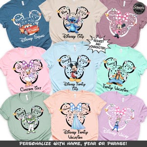 May include: A collection of colorful t-shirts featuring Disney characters and phrases. Each shirt has a Mickey Mouse head design with a character image, the year 2026, and text like "Disney Trip" or "Family Vacation". The shirts are available in various colors.