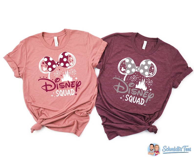 Puede incluir: Dos camisetas con una silueta blanca de orejas de Mickey Mouse con un lazo y el texto "Disney Squad" en blanco con un castillo rosa y fuegos artificiales. La camiseta de la izquierda es de color rosa polvoriento y la camiseta de la derecha es de color burdeos.