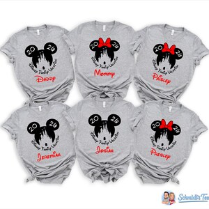 K&ouml;nnte beinhalten: Sechs graue T-Shirts mit einem Disney Family Vacation-Design. Jedes Shirt zeigt einen Mickey Mouse-Kopf mit dem Jahr 2020, eine Schlosssilhouette und den Namen eines Familienmitglieds in Rot oder Schwarz. Ein Shirt hat eine rote Schleife.