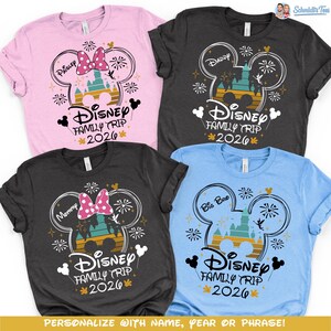 May include: Four short-sleeved t-shirts in pink, charcoal, and blue, each featuring a Disney-themed design. The design includes a Mickey Mouse head outline, a castle, fireworks, and the text "Disney Family Trip 2026".