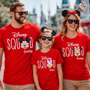 May include: Red t-shirts with the text "Disney Squad" and Mickey and Minnie Mouse graphics. The shirts are worn by a family, with the text "Daddy", "Mommy", and a name on each shirt. The family is wearing sunglasses and mouse ears.
