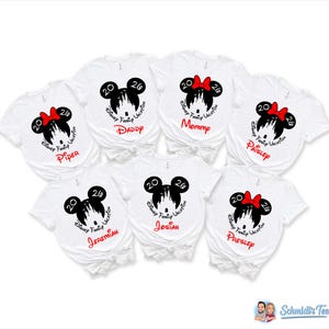 K&ouml;nnte beinhalten: Wei&szlig;e T-Shirts mit schwarzen Mickey-Mouse-Designs und roten Schleifen. Jedes Shirt hat einen Namen in Rot aufgedruckt, darunter "Daddy", "Mommy" und andere Namen. Die Shirts tragen auch den Text "Disney Family Vacation 20".