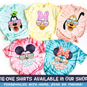 May include: Five tie-dye t-shirts featuring different Disney characters wearing sunglasses. The shirts are available in a variety of colors, including blue, yellow, orange, red, and green. The text "Best Day Ever" is printed on two of the shirts.
