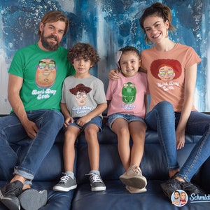 May include: A family of four wearing matching t-shirts with a cartoon character and the text "Best Day Ever". The shirts are green, grey, pink, and peach. The family is sitting on a blue couch.