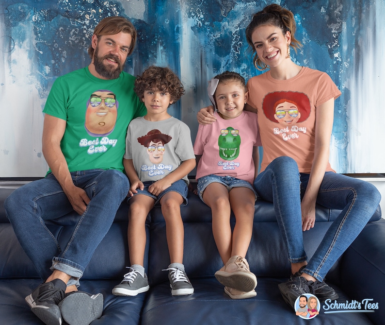May include: A family of four wearing matching t-shirts with a cartoon character and the text "Best Day Ever". The shirts are green, grey, pink, and peach. The family is sitting on a blue couch.