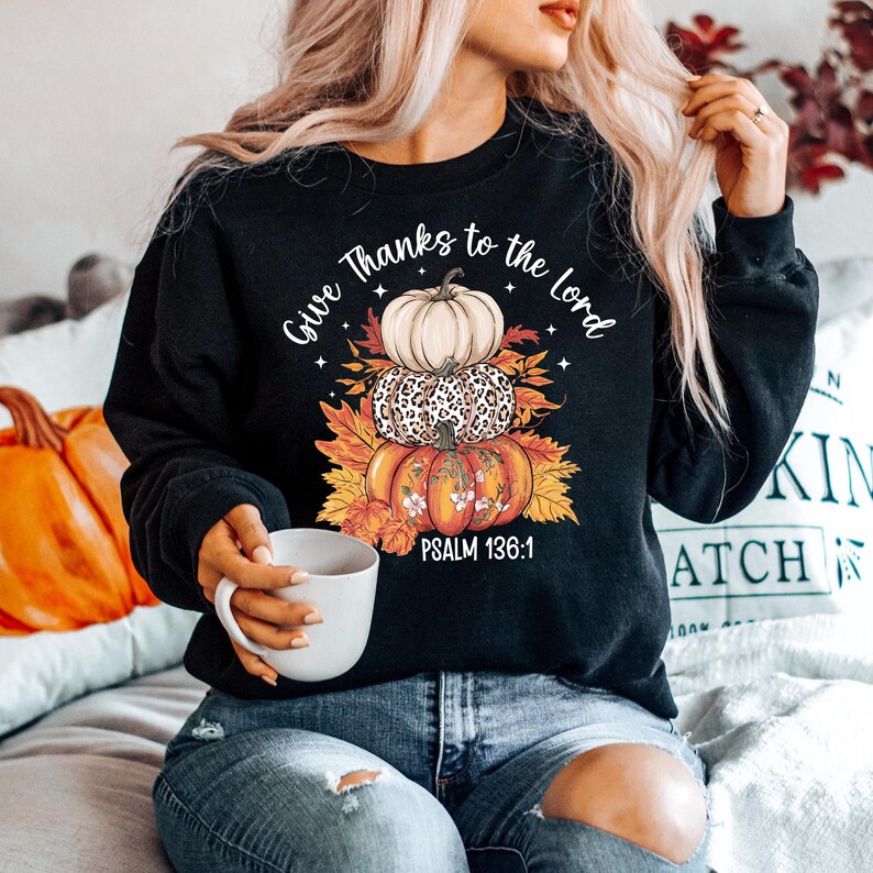 May include: Black sweatshirt with a stacked pumpkin graphic. The pumpkins are white, leopard print, and orange, with fall leaves. Text reads "Give Thanks to the Lord" and "Psalm 136:1".