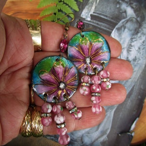 May include: A pair of dangle earrings with pink and white glass beads and a blue and green enamel flower charm. The flower charm has gold accents and a pink center.