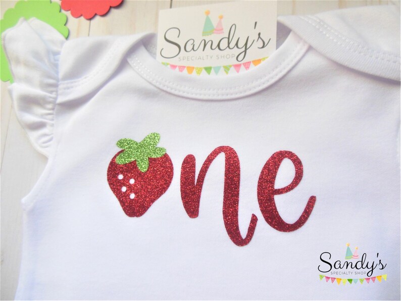 May include: White baby onesie with red glitter 'one' and a red glitter strawberry with green leaves.