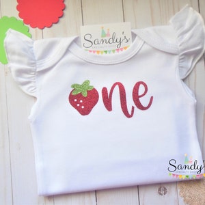 May include: White baby onesie with a red glitter strawberry and the word "one" in red glitter. The onesie has ruffled sleeves.