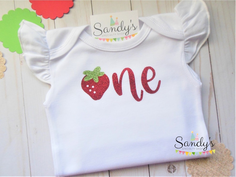 May include: White baby onesie with red glitter 'one' and a red glitter strawberry with green leaves.