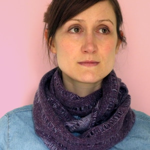 Puede incluir: Una mujer con una bufanda de punto infinita de color morado y una camisa vaquera. La bufanda es gruesa y tiene un patrón texturizado.