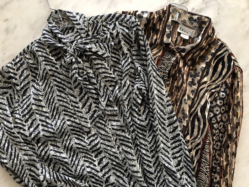 May include: Two long-sleeved blouses with animal print patterns. One blouse has a black and white chevron pattern, the other has a brown, black, and white zebra and leopard print. The blouse with the zebra and leopard print has a label that says "Expos&eacute;".