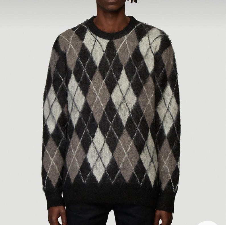 May include: A black, brown, and white argyle sweater. The sweater features a classic diamond pattern in shades of black, brown, grey, and white. The sweater has a crew neck and long sleeves.