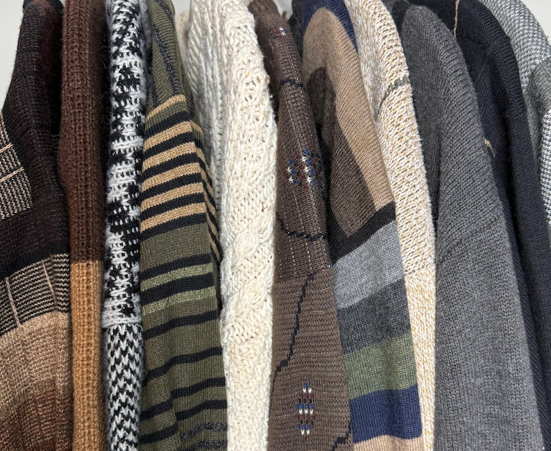 May include: A collection of various sweaters hanging on a rack. The sweaters display a range of colors and patterns, including stripes, cable knits, and geometric designs. The color palette includes brown, beige, green, and gray tones, offering a variety of textures and styles.