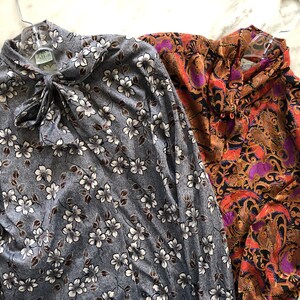 May include: Two long-sleeved blouses, one with a floral print in shades of gray and white, and the other with a paisley print in shades of orange, purple, and black.
