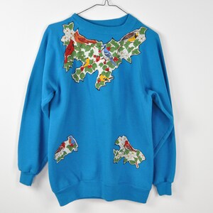 May include: A blue sweatshirt with a colourful embroidered design of birds and flowers on the front. The design is in the shape of a bird.