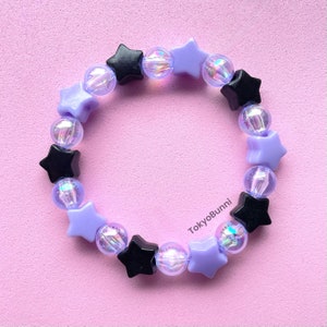 May include: A purple and black star-shaped beaded bracelet. The bracelet is made with iridescent beads and features alternating black and purple star-shaped beads.