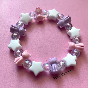 May include: A purple and pink beaded bracelet with star and cat charms. The bracelet is made with iridescent beads and has a pink and purple cat charm.