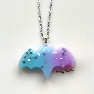 May include: A silver chain necklace with a blue and purple ombre resin bat pendant. The bat has silver glitter stars embedded in the resin.