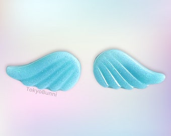 May include: A pair of light blue glitter angel wings. The wings are made of resin and have a sparkly finish.