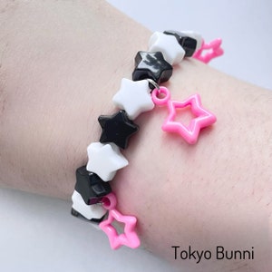 May include: A black, white, and pink star-shaped beaded bracelet with pink star charms. The bracelet is on a person's wrist. "Tokyo Bunni" is written in white text on a black background.