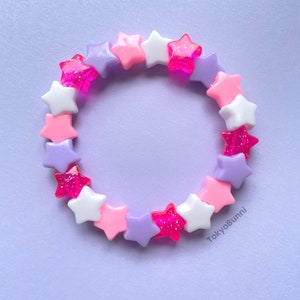 May include: A pink, purple, and white star-shaped beaded bracelet. The beads are made of plastic and have a glittery finish.