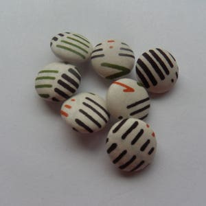 Peut inclure: Sept boutons ronds avec un fond blanc et des motifs géométriques noirs, verts et orange.
