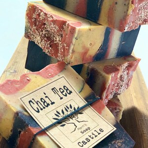 May include: A stack of handmade soap bars with a brown, red, yellow, and black marbled design. The top bar has a label that reads "Chai Tea" and "Mart's Soap Castile".