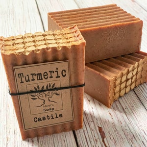 Puede incluir: Tres barras de jabón marrón con una etiqueta que dice "Turmeric Castile Marti's Soap".