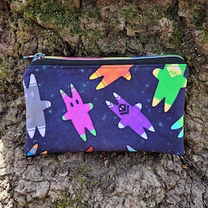 Puede incluir: Una bolsa negra con cremallera con un estampado colorido de tem&aacute;tica espacial con varios personajes de dibujos animados. Los personajes son de diferentes colores y tienen forma de estrella.