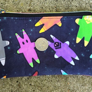 Puede incluir: Una bolsa negra con cremallera con un estampado de tem&aacute;tica espacial con figuras de dibujos animados coloridas sobre un fondo azul oscuro con estrellas blancas.