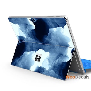 Könnte beinhalten: Eine Laptop-Haut im blauen und weißen Aquarell-Design für einen Microsoft Surface Laptop. Die Haut bedeckt die Ober- und Unterseite des Laptops und hat einen blauen Stift daneben.