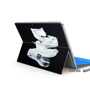 May include: A black and white laptop with a white paint splatter design. The laptop is closed and the screen is facing away from the viewer. The laptop is sitting on a blue surface.