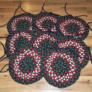 May include: A set of eight round braided rugs in black, green, red, and white. The rugs are made of thick, woven fabric and have a fringed edge. Each rug has a black string attached to it.