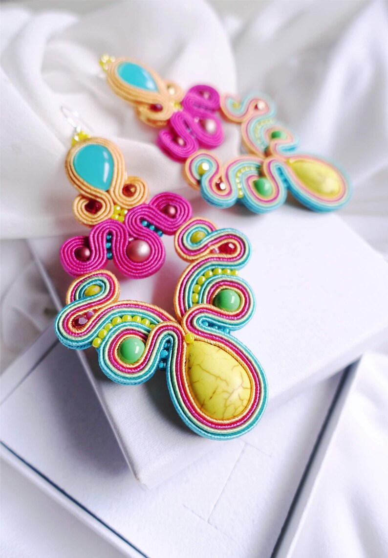 Pu&ograve; includere: Un paio di orecchini colorati con accenti turchese, rosa, giallo e verde. Gli orecchini sono realizzati con filo intrecciato e presentano grandi pietre a forma di goccia.