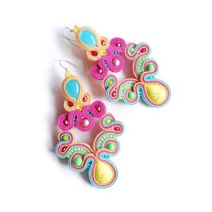 Pu&ograve; includere: Un paio di orecchini pendenti colorati con accenti turchese, giallo, rosa e verde. Gli orecchini sono realizzati con filo intrecciato e presentano una pietra a forma di lacrima.