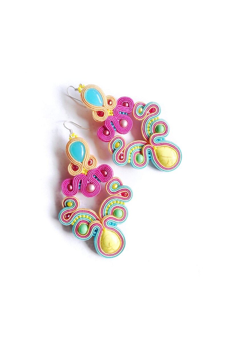 Pu&ograve; includere: Un paio di orecchini pendenti colorati con accenti turchese, giallo, rosa e verde. Gli orecchini sono realizzati con filo intrecciato e presentano una pietra a forma di lacrima.